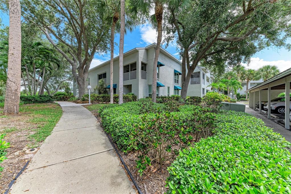 A concrete walkway leads toward a multi-story apartment building surrounded by trees and landscaping — 309 108TH STREET W UNIT 309, BRADENTON, FL