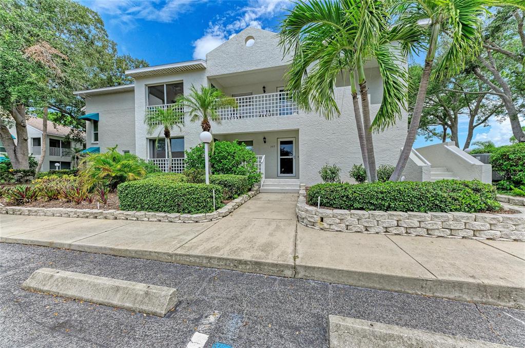 A two-story stucco building with a concrete walkway, landscaping, and palm trees in front — 309 108TH STREET W UNIT 309, BRADENTON, FL