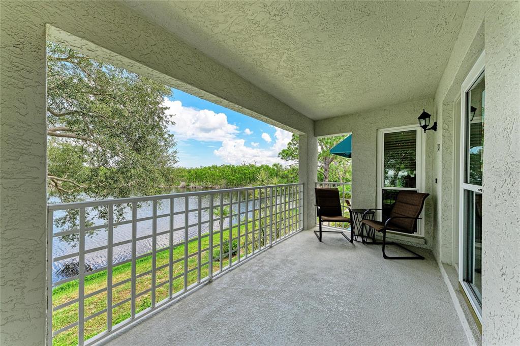 A covered balcony with a white metal railing overlooks a lake and grassy yard — 309 108TH STREET W UNIT 309, BRADENTON, FL