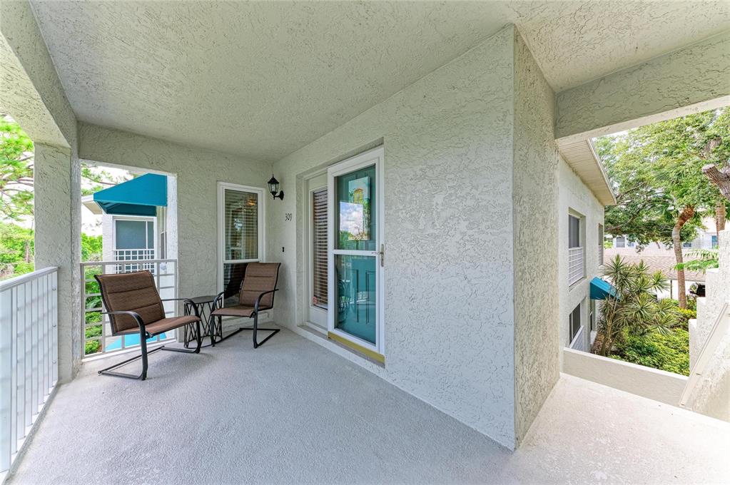 A covered balcony features a teal door, two chairs, and a small table — 309 108TH STREET W UNIT 309, BRADENTON, FL