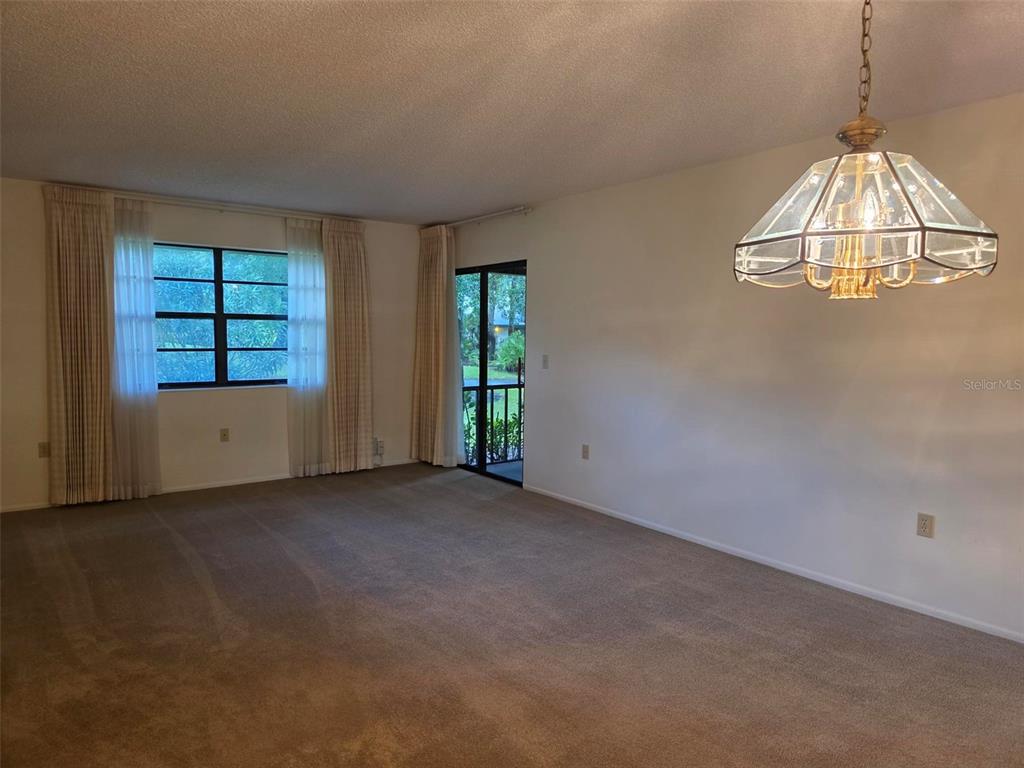 An empty living room features beige carpeting, a large window with curtains, and a chandelier — 2923 FIG COURT, PALM HARBOR, FL