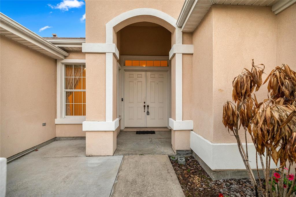 A beige stucco house exterior features a covered entryway with double doors and a window — 9512 SE 124TH LOOP, SUMMERFIELD, FL