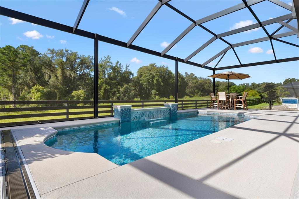A covered patio features a swimming pool, outdoor kitchen, and wicker furniture under a screen enclosure — 504 BEDMINSTER WAY, THE VILLAGES, FL
