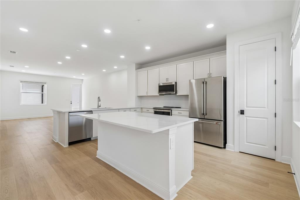 A modern kitchen features white cabinetry, stainless steel appliances, a center island, and light wood flooring — 17736 BROADLEAF LOOP, VENICE, FL