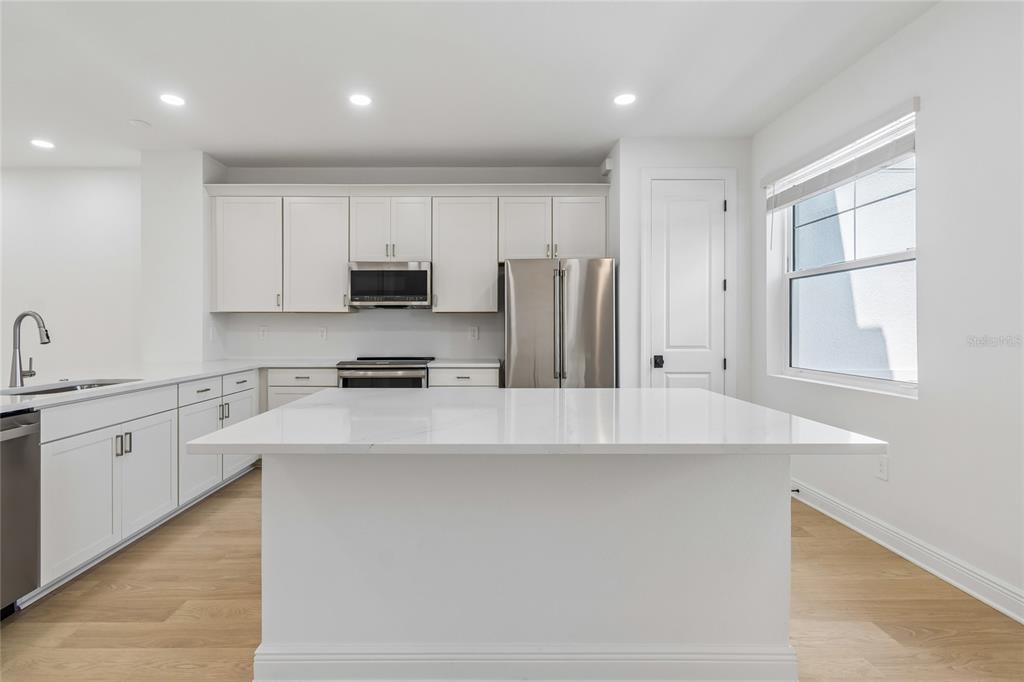 A modern kitchen features white cabinetry, stainless steel appliances, and a large white quartz island — 17736 BROADLEAF LOOP, VENICE, FL