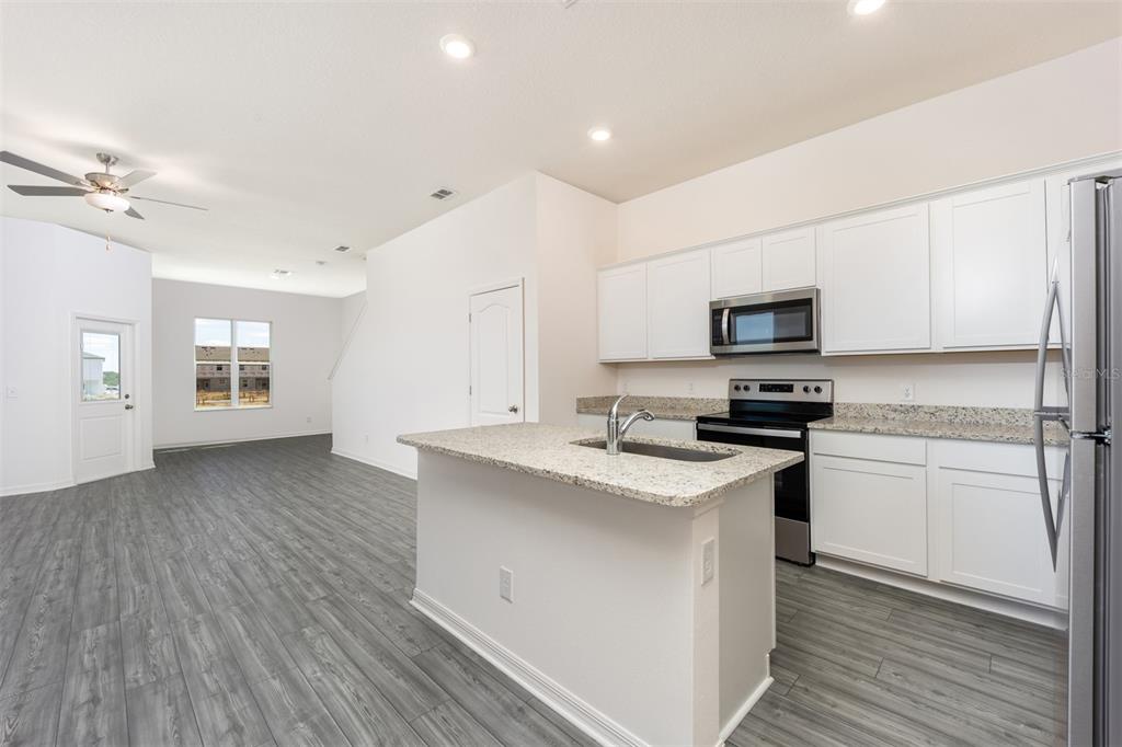 A kitchen with white cabinets, granite countertops, and an island overlooks an open living area — 678 POPPY LANE, DUNDEE, FL
