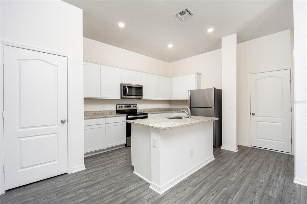 A kitchen features white cabinets, granite countertops, stainless steel appliances, and gray wood-look flooring — 678 POPPY LANE, DUNDEE, FL