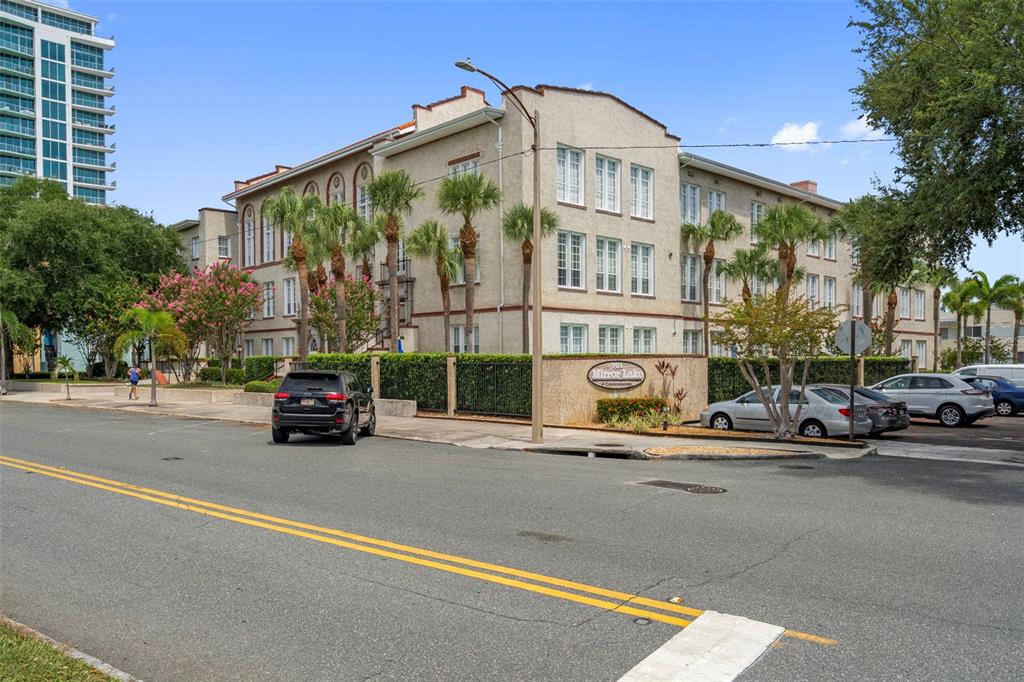 A multi-story tan apartment building with palm trees and parked cars in front — 701 MIRROR LAKE DRIVE N UNIT 317, ST PETERSBURG, FL