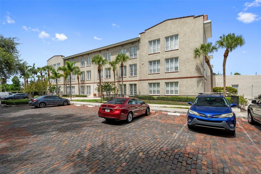 A multi-story beige building with a brick parking lot and several parked cars — 701 MIRROR LAKE DRIVE N UNIT 317, ST PETERSBURG, FL