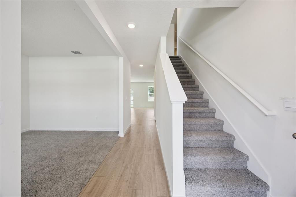 An interior view shows a carpeted living area, a hallway with wood-look flooring, and stairs — 1139 GULL DRIVE, APOPKA, FL