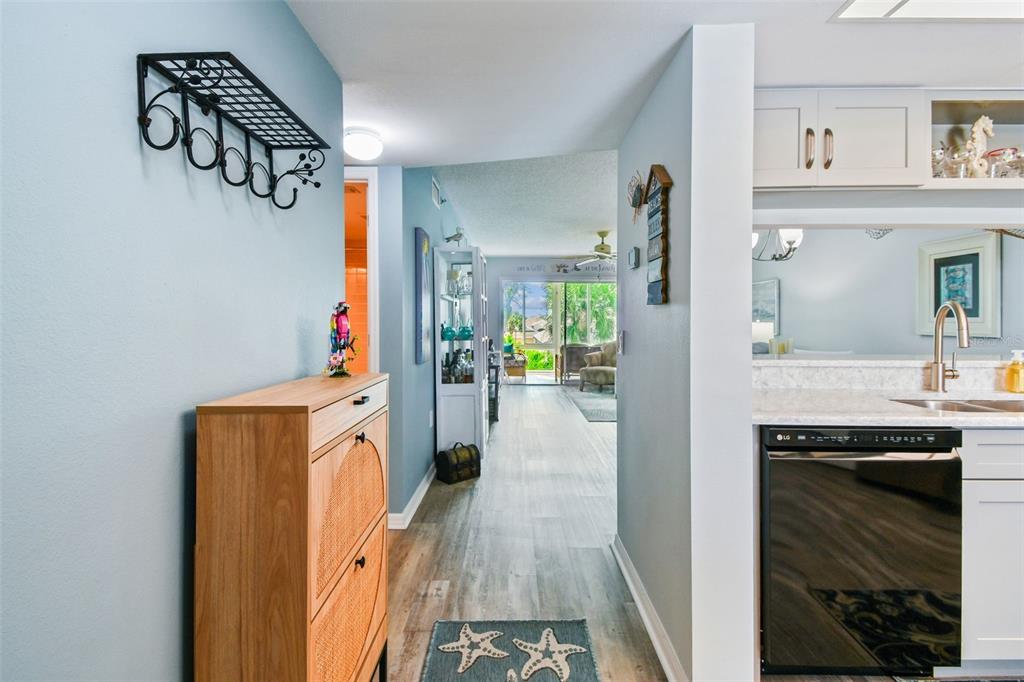 A hallway with light blue walls leads past a wooden cabinet toward a sunlit living area — 7301 29TH AVE DR W UNIT 202, BRADENTON, FL