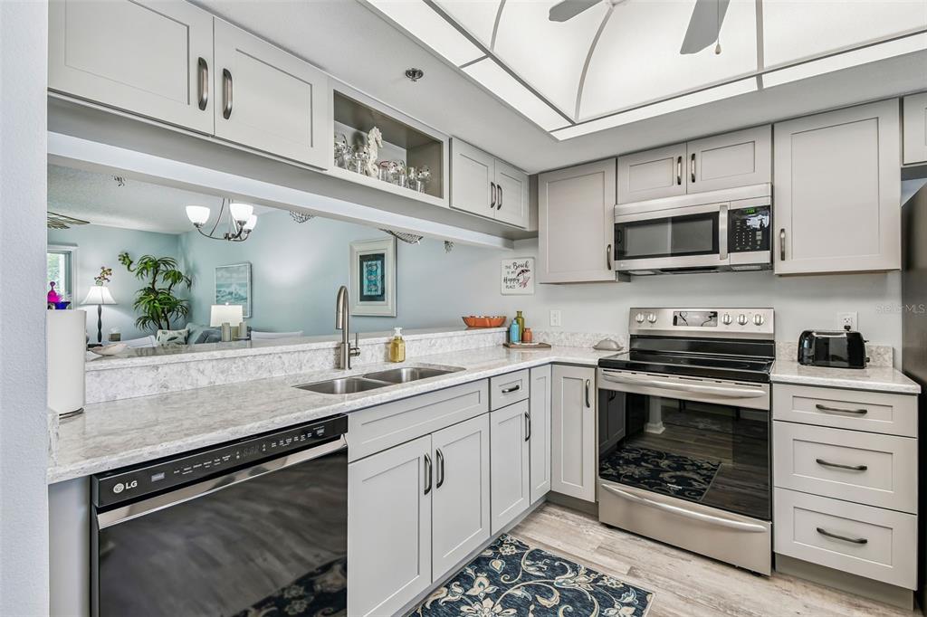 A kitchen features light gray cabinets, stainless steel appliances, and a pass-through window to the living area — 7301 29TH AVE DR W UNIT 202, BRADENTON, FL