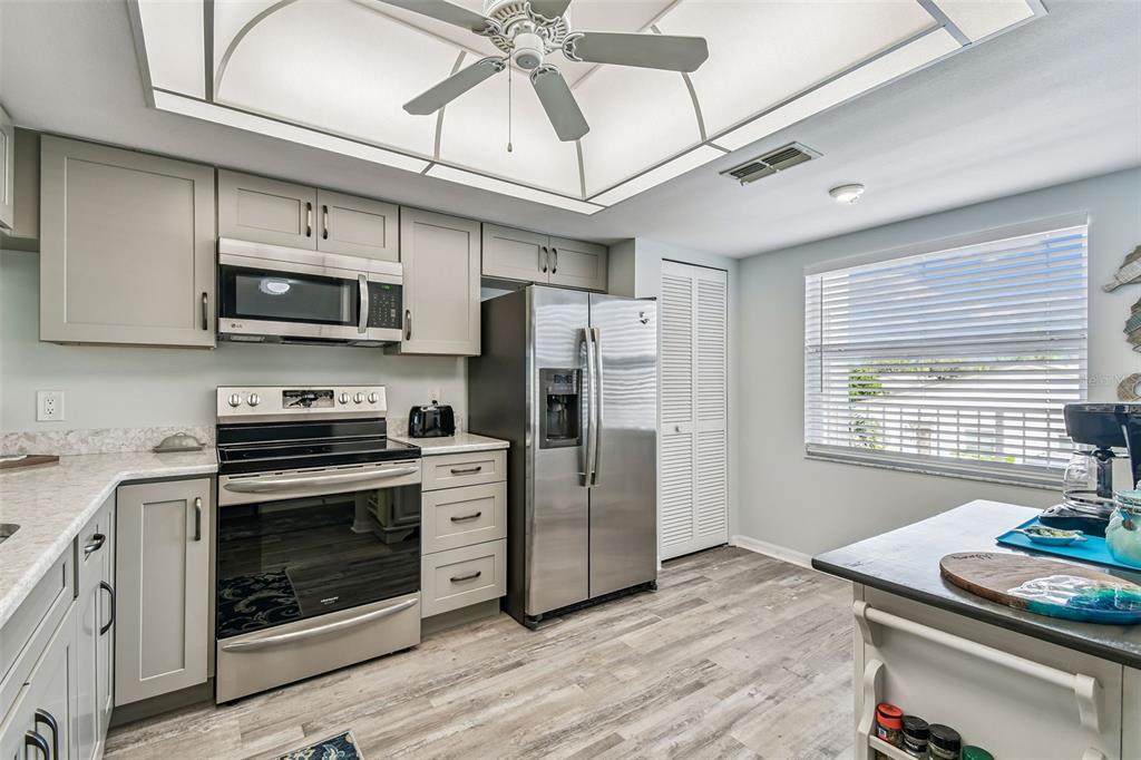 A kitchen features gray cabinets, stainless steel appliances, a ceiling fan, and wood-look flooring — 7301 29TH AVE DR W UNIT 202, BRADENTON, FL