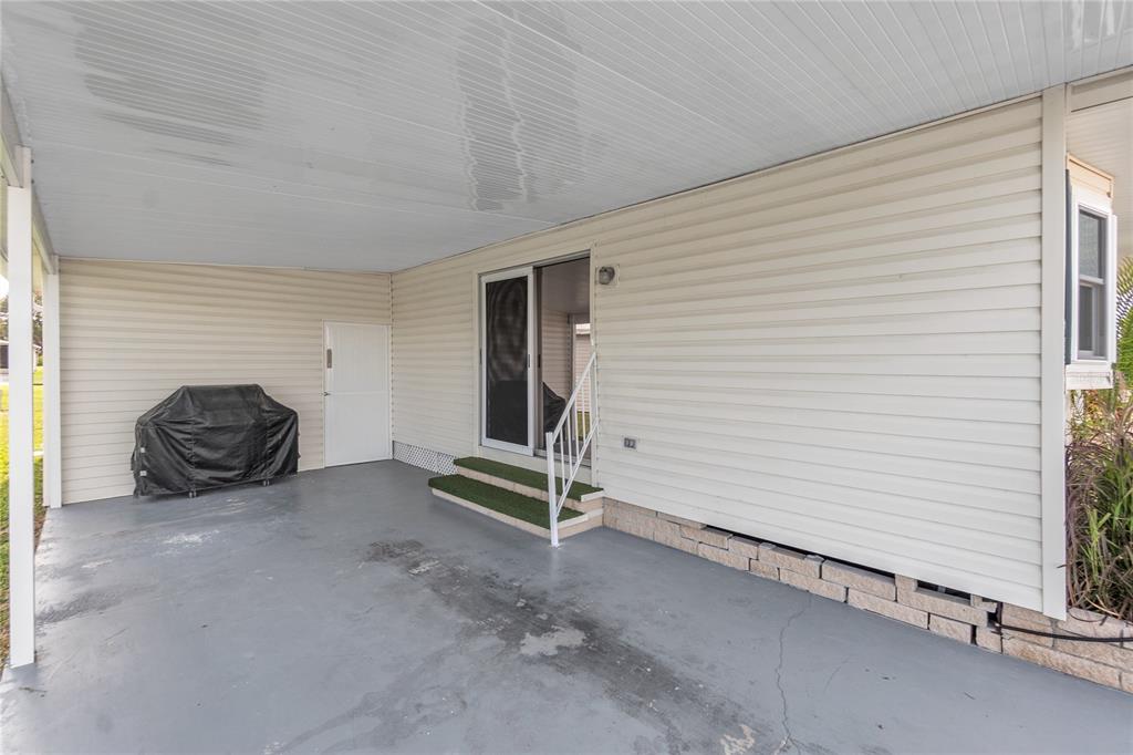 A covered concrete patio features beige vinyl siding, a sliding glass door, and a grill — 1535 45TH AVENUE DRIVE E, ELLENTON, FL