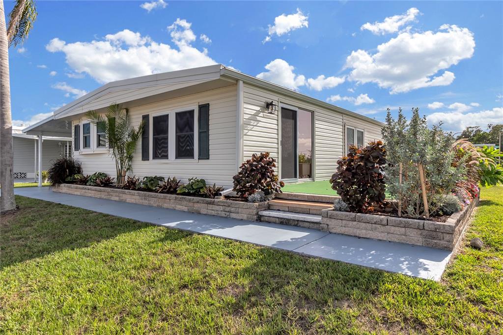 A light-colored manufactured home features a concrete walkway, stone retaining walls, and landscaped garden beds — 1535 45TH AVENUE DRIVE E, ELLENTON, FL