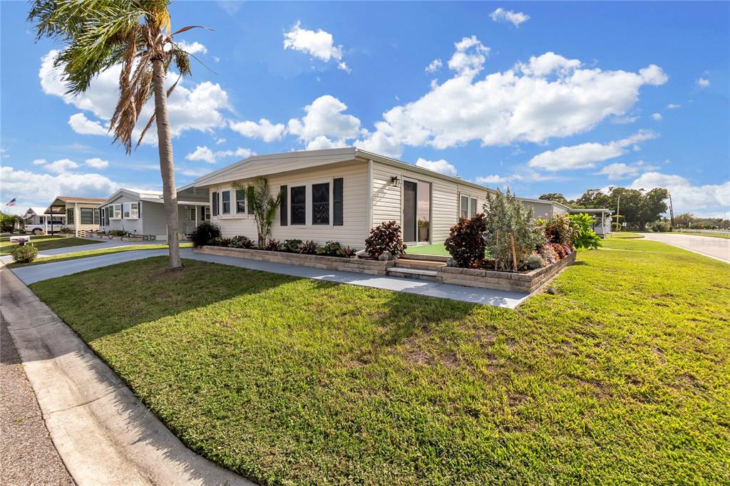 A single-story manufactured home with light siding, a palm tree, and landscaped garden beds — 1535 45TH AVENUE DRIVE E, ELLENTON, FL