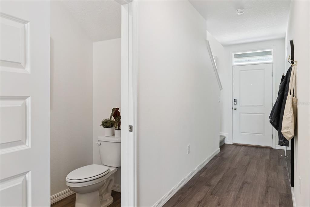A view of a hallway with wood-look flooring, a half bathroom, and a front door — 4276 BUTTERSCOTCH CIRCLE, LAKELAND, FL