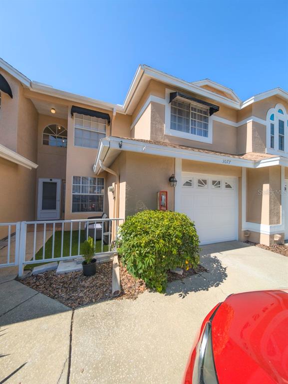 A two-story townhouse exterior features a white garage door, a small fenced patio, and beige siding — 3077 BRANCH DRIVE, CLEARWATER, FL