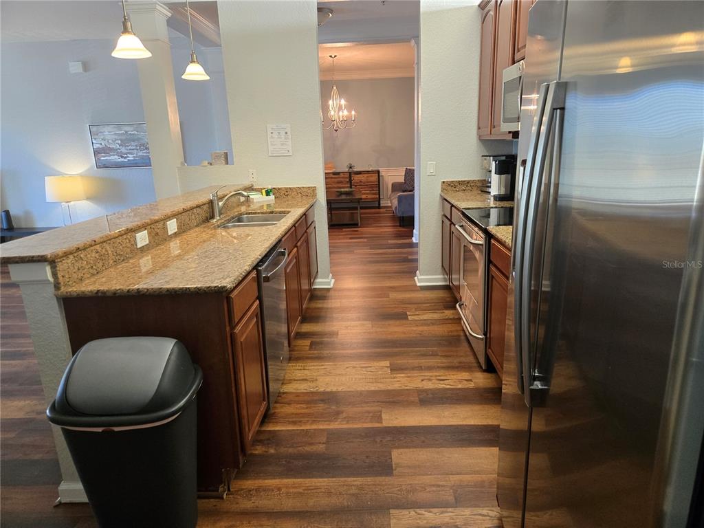 A kitchen features wood cabinets, granite countertops, stainless steel appliances, and wood-look flooring — 5049 SHOREWAY LOOP UNIT 30101, ORLANDO, FL