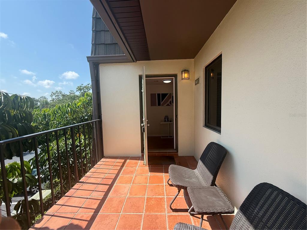 A tiled balcony features a metal railing, two wicker chairs, and an open doorway — 1645 SPOONBILL LANE UNIT C, NAPLES, FL