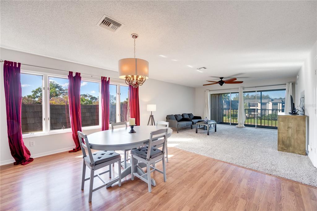 A dining area with wood flooring transitions into a carpeted living room with sliding glass doors — 1645 SPOONBILL LANE UNIT C, NAPLES, FL