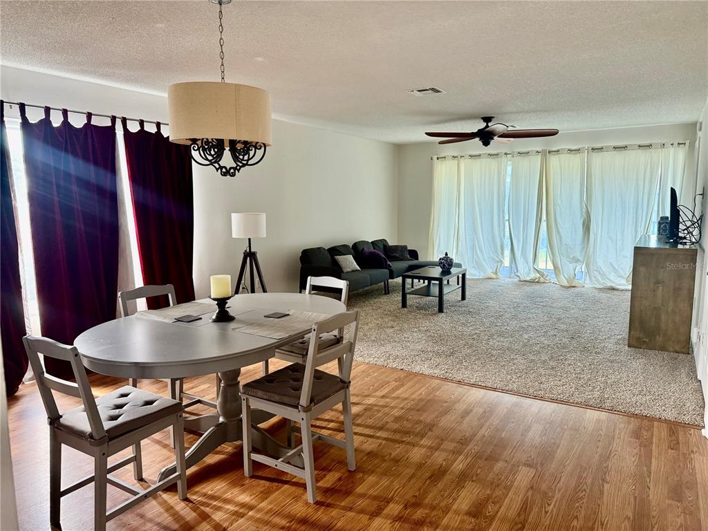 A dining area with a wooden table and chairs transitions into a carpeted living room — 1645 SPOONBILL LANE UNIT C, NAPLES, FL