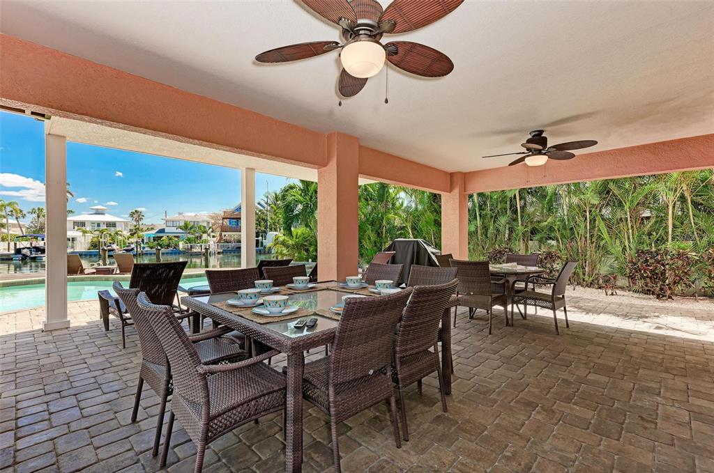 A covered outdoor patio features a dining set, ceiling fans, and a view of a canal — 203 N HARBOR DRIVE, HOLMES BEACH, FL