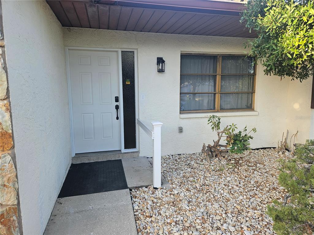The exterior entrance features a white front door, a side window, and a gravel yard — 11557 124TH TERRACE, LARGO, FL