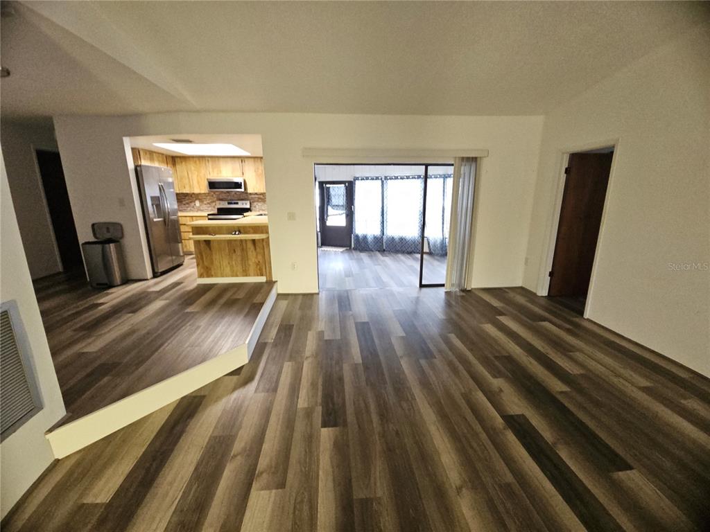 A living area with wood-look flooring leads to a kitchen and a sunroom — 11557 124TH TERRACE, LARGO, FL