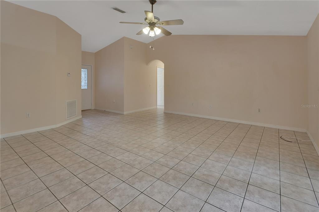 An empty room features light-colored tile flooring, beige walls, and a vaulted ceiling with a fan — 2249 HONTOON ROAD, DELAND, FL