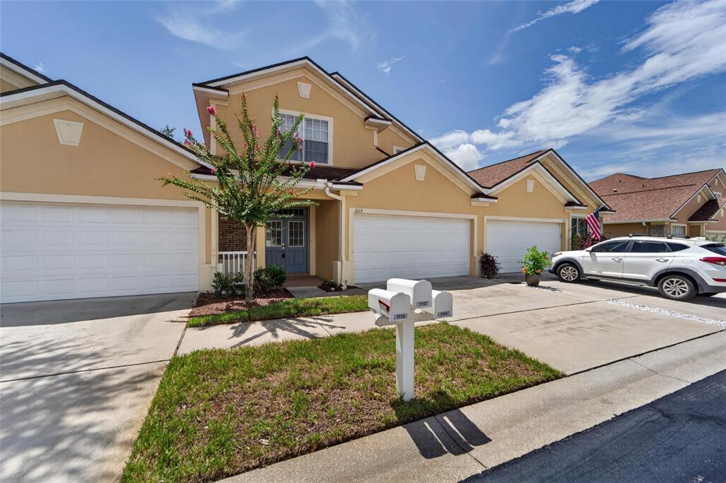 A multi-unit residential building with beige stucco siding, white garage doors, and a shared mailbox — 1113 SAVANNAH LANDINGS AVENUE, VALRICO, FL