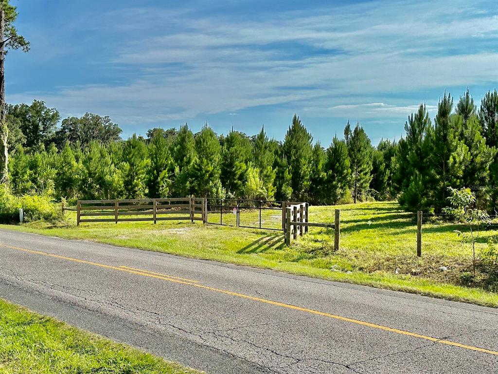 A paved road runs alongside a grassy lot enclosed by a wooden and wire fence — Parcel B NW 160TH AVENUE, MORRISTON, FL