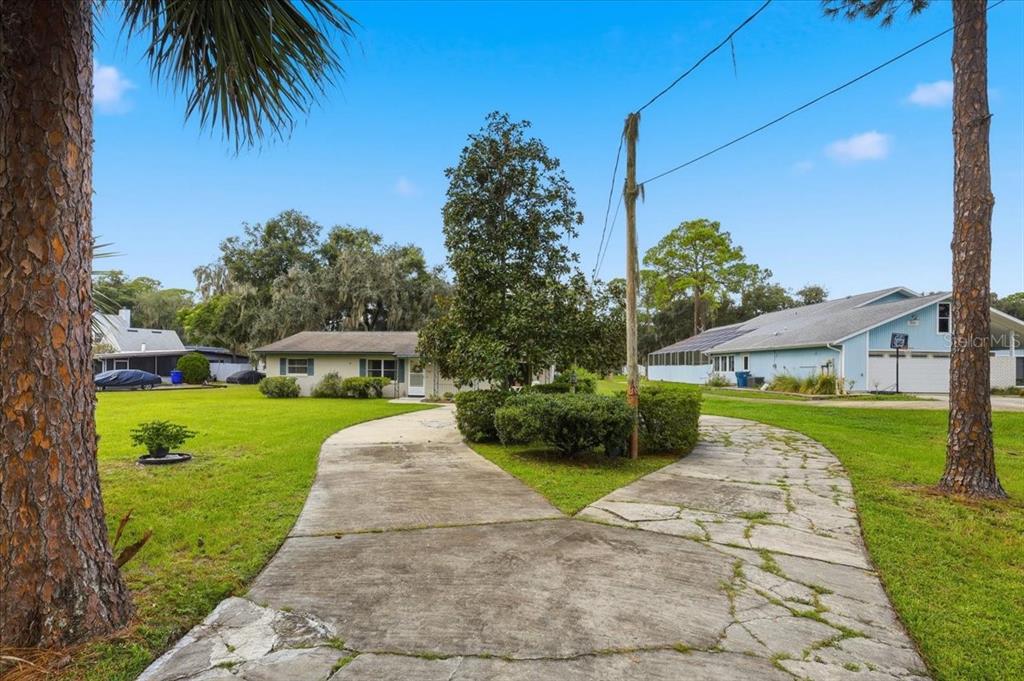 A concrete driveway leads to a single-story house with a large lawn and mature trees — 2228 RIVER RIDGE ROAD, DELAND, FL