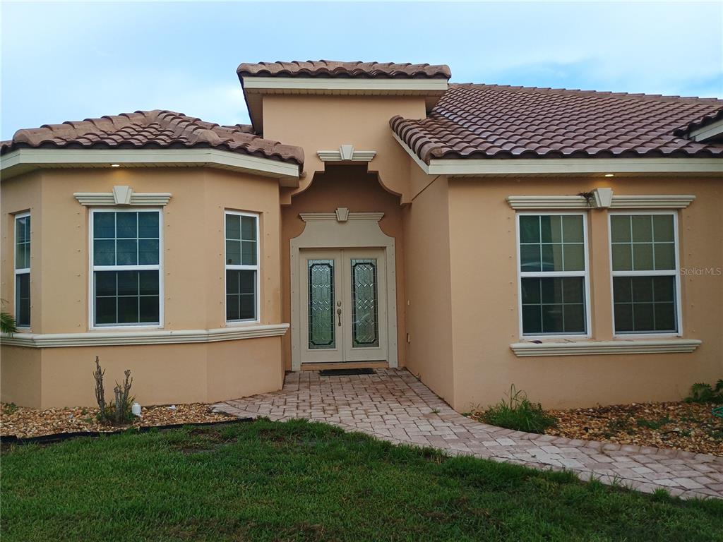 A tan, single-story house with a tiled roof and a brick walkway leading to double doors — 4394 PRESERVATION CIRCLE, MELBOURNE, FL