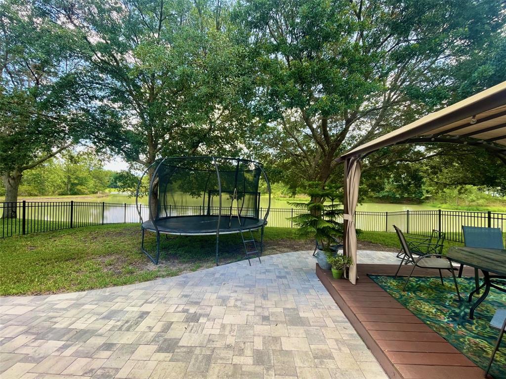 A backyard patio features a trampoline, a covered deck area, and a view of a pond — 4522 LISETTE CIRCLE, BROOKSVILLE, FL
