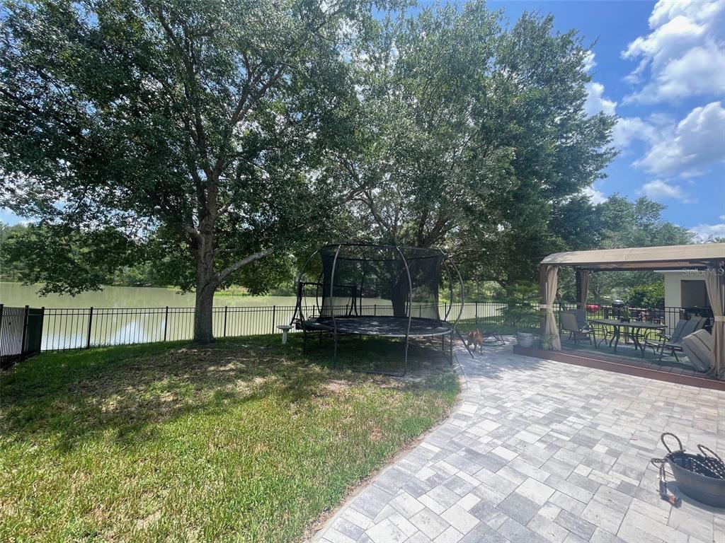 A backyard features a paved patio, a trampoline, and a fenced lawn overlooking a lake — 4522 LISETTE CIRCLE, BROOKSVILLE, FL