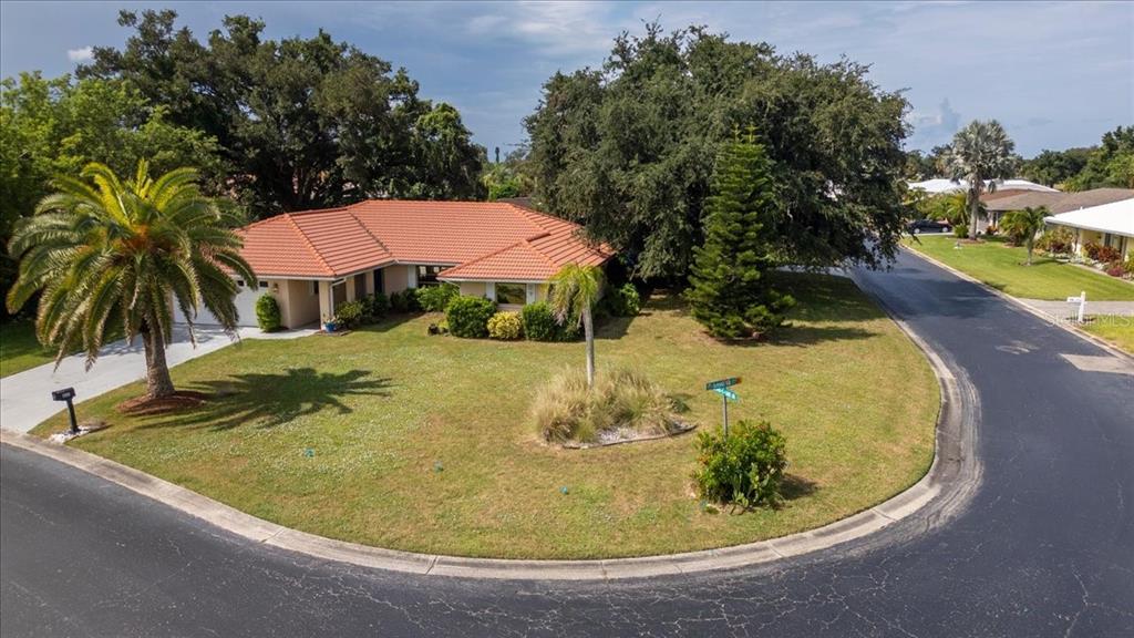 A single-story house with a terracotta tile roof sits on a corner lot with landscaping — 1608 BOB O LINK DRIVE, VENICE, FL