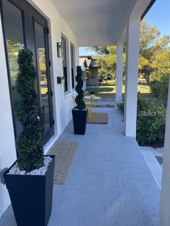 A covered front porch features two spiral topiary plants in black planters and yellow bistro furniture — 5101 12TH AVENUE N, ST PETERSBURG, FL