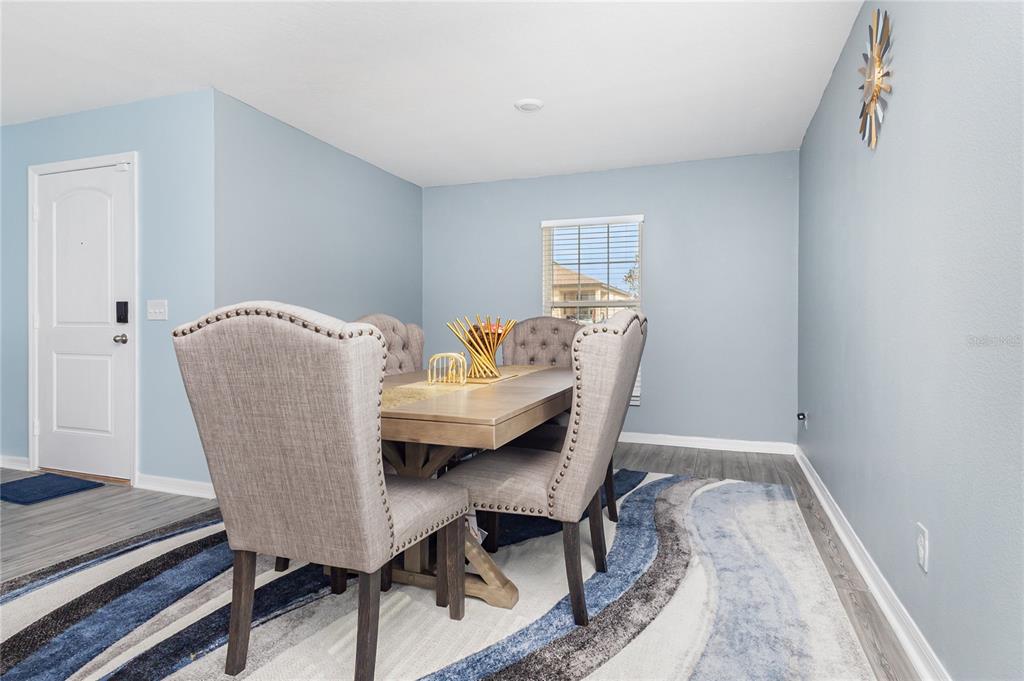 A dining room features a wooden table, upholstered chairs, a blue patterned rug, and light blue walls — 1760 CANAAN LOOP, DUNDEE, FL