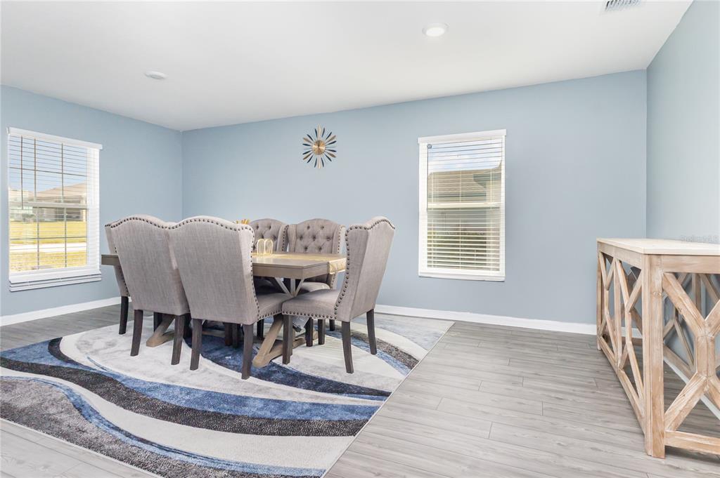 A dining room features light blue walls, gray wood-look flooring, and a patterned area rug — 1760 CANAAN LOOP, DUNDEE, FL
