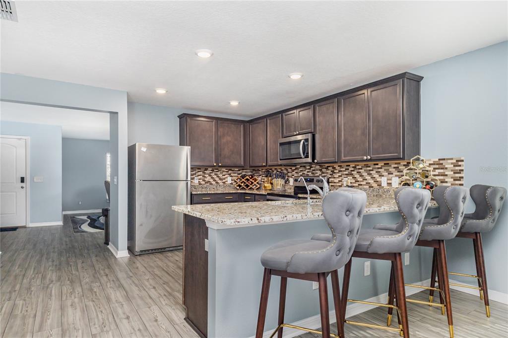 A kitchen features dark wood cabinets, granite countertops, stainless steel appliances, and three gray barstools — 1760 CANAAN LOOP, DUNDEE, FL