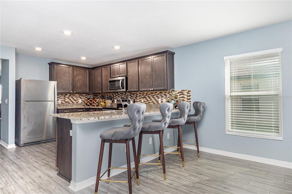 A kitchen features dark wood cabinets, granite countertops, a stainless steel refrigerator, and four barstools — 1760 CANAAN LOOP, DUNDEE, FL