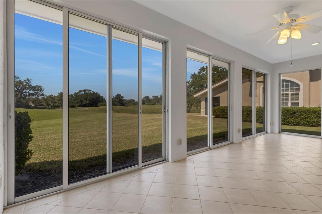 A sunroom with tile flooring, a ceiling fan, and large sliding glass doors overlooking a golf course — 4044 PENSHURST PARK, SARASOTA, FL
