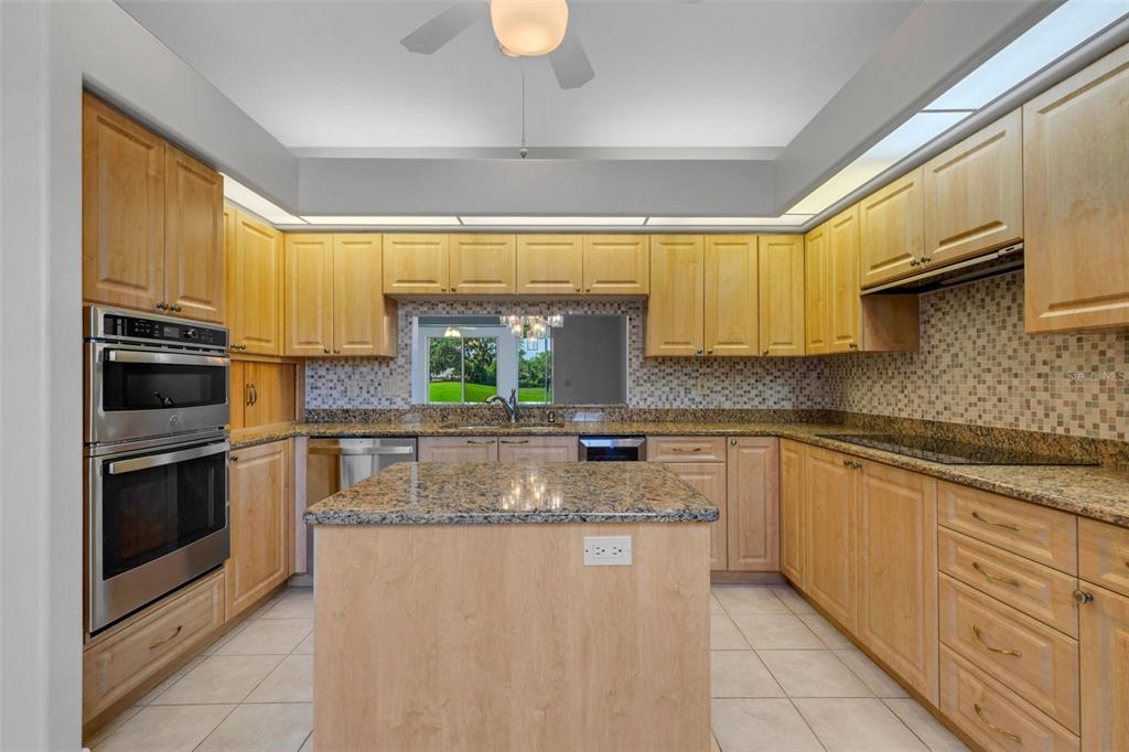 A kitchen features light wood cabinets, granite countertops, a central island, and stainless steel appliances — 4044 PENSHURST PARK, SARASOTA, FL