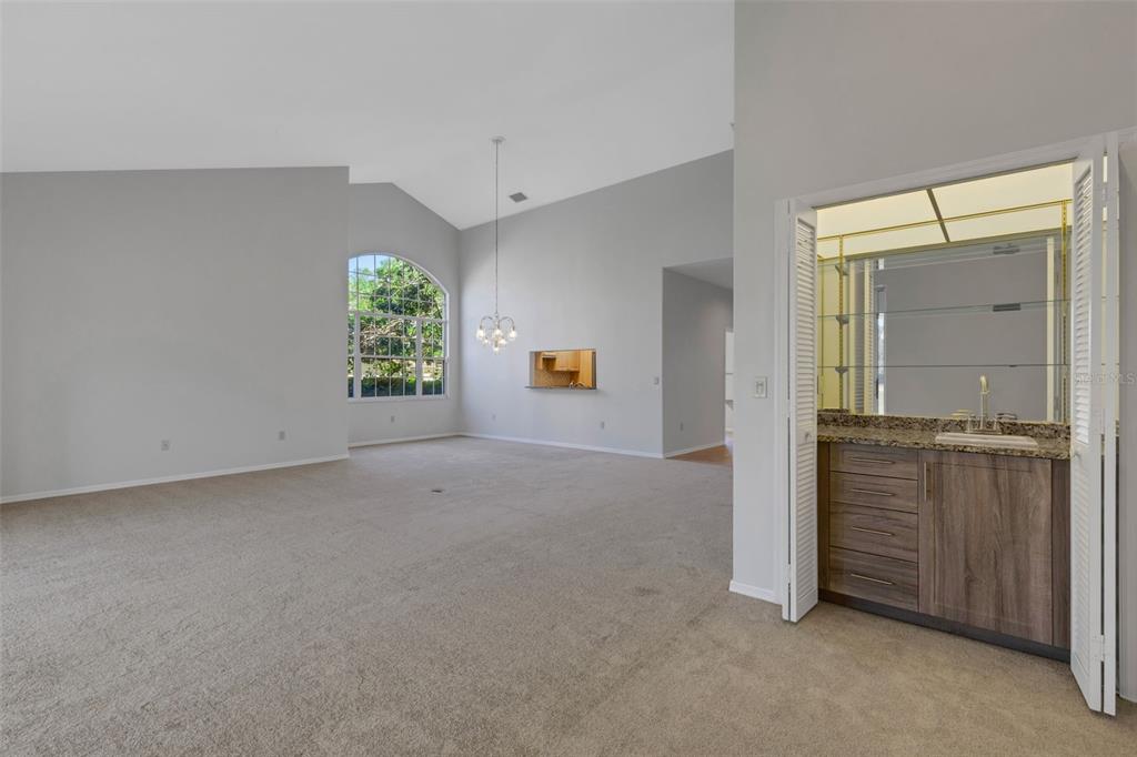 A spacious living room with vaulted ceilings, a large arched window, and a wet bar — 4044 PENSHURST PARK, SARASOTA, FL