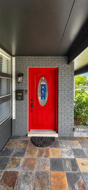 A red front door is set in a gray brick wall above a slate tile porch — 1505 ARROWHEAD DRIVE, SUN CITY CENTER, FL