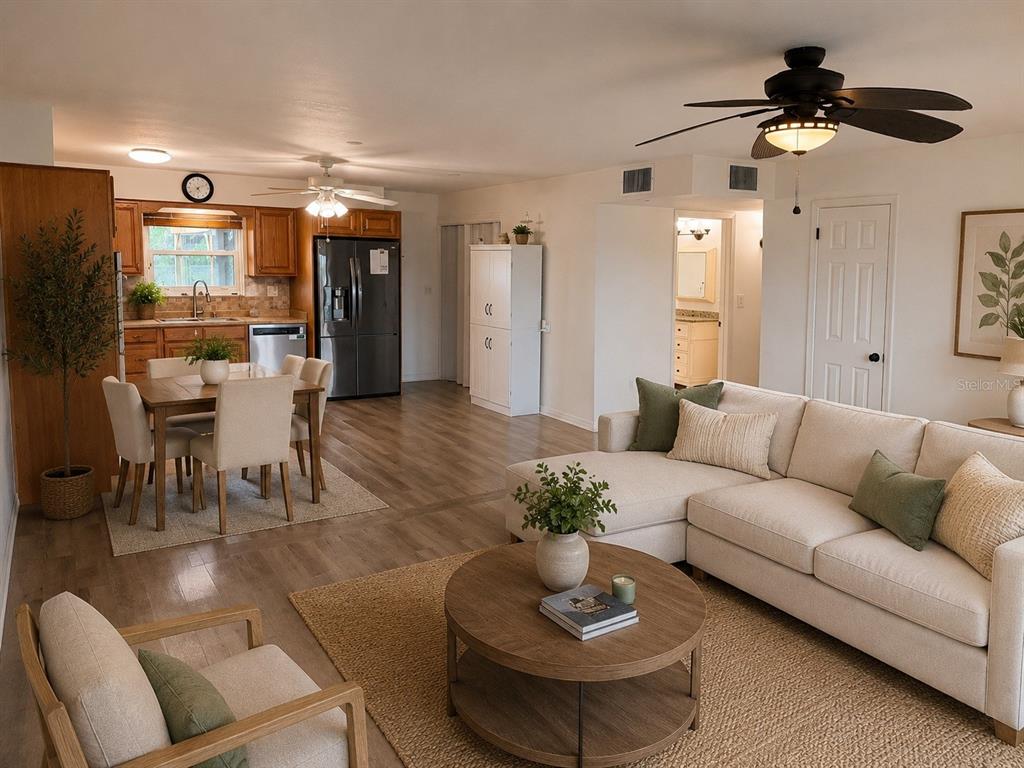 An open-concept living and dining area features light wood flooring, a sectional sofa, and kitchen — 1505 ARROWHEAD DRIVE, SUN CITY CENTER, FL