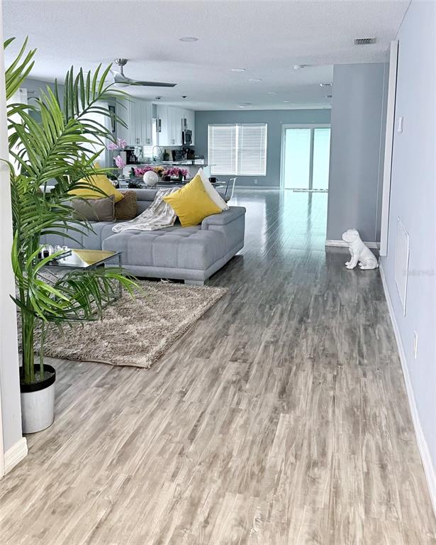 An open-concept living room features a grey sectional sofa, wood-look flooring, and a kitchen beyond — 4440 BLEASDALE AVENUE, ORLANDO, FL