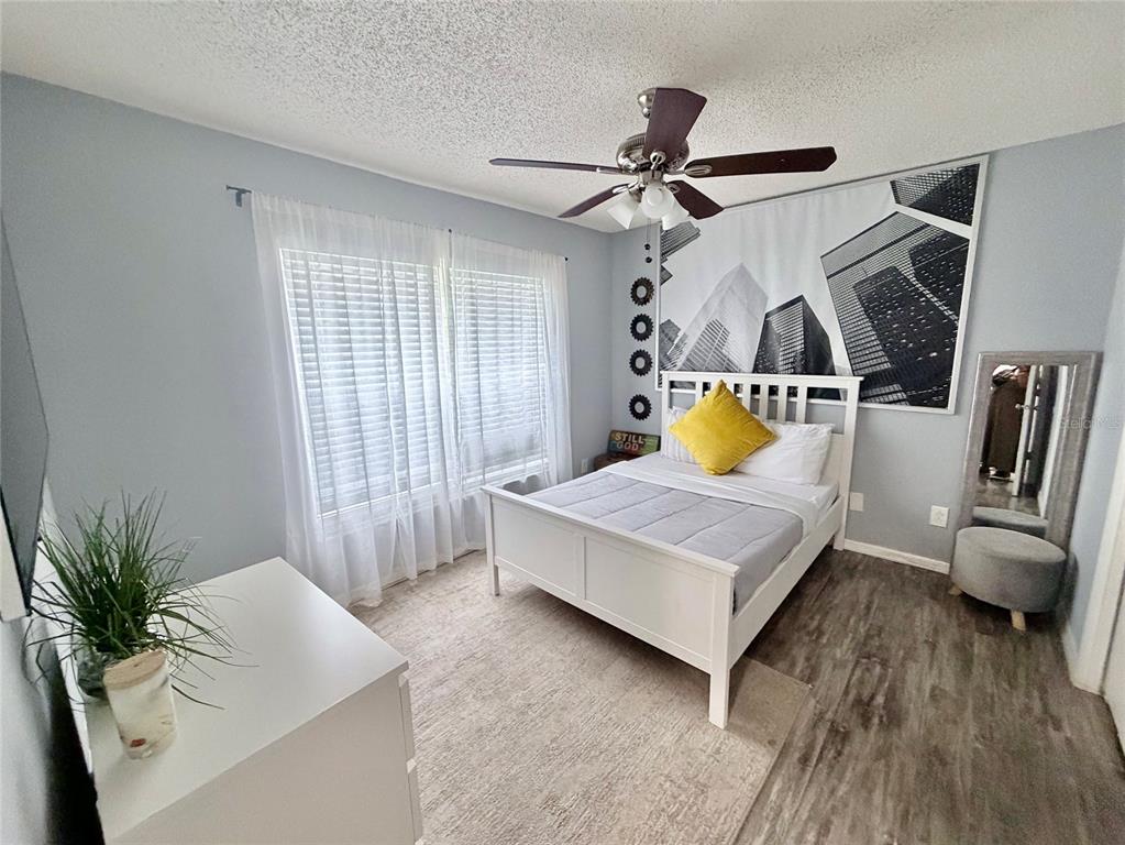 A bedroom features a white bed, a city skyline wall tapestry, and light wood flooring — 4440 BLEASDALE AVENUE, ORLANDO, FL