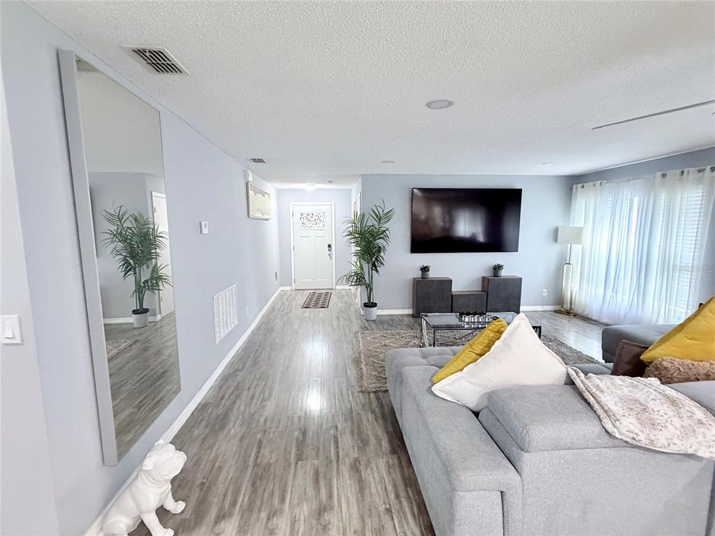 A living room features light wood-look flooring, a large wall-mounted television, and a gray sectional — 4440 BLEASDALE AVENUE, ORLANDO, FL
